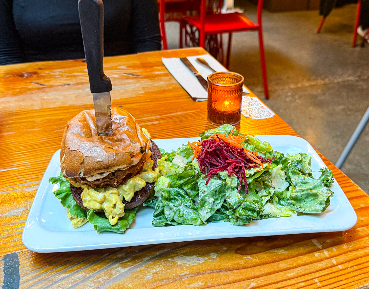A plate of food consists of a burger and leafy vegetables.