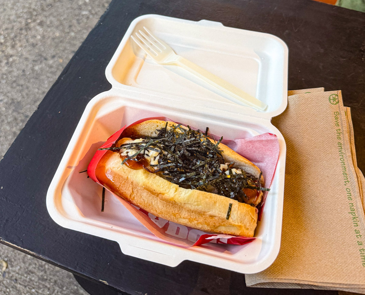 A sandwhiched hotdog topped with seaweed flakes.