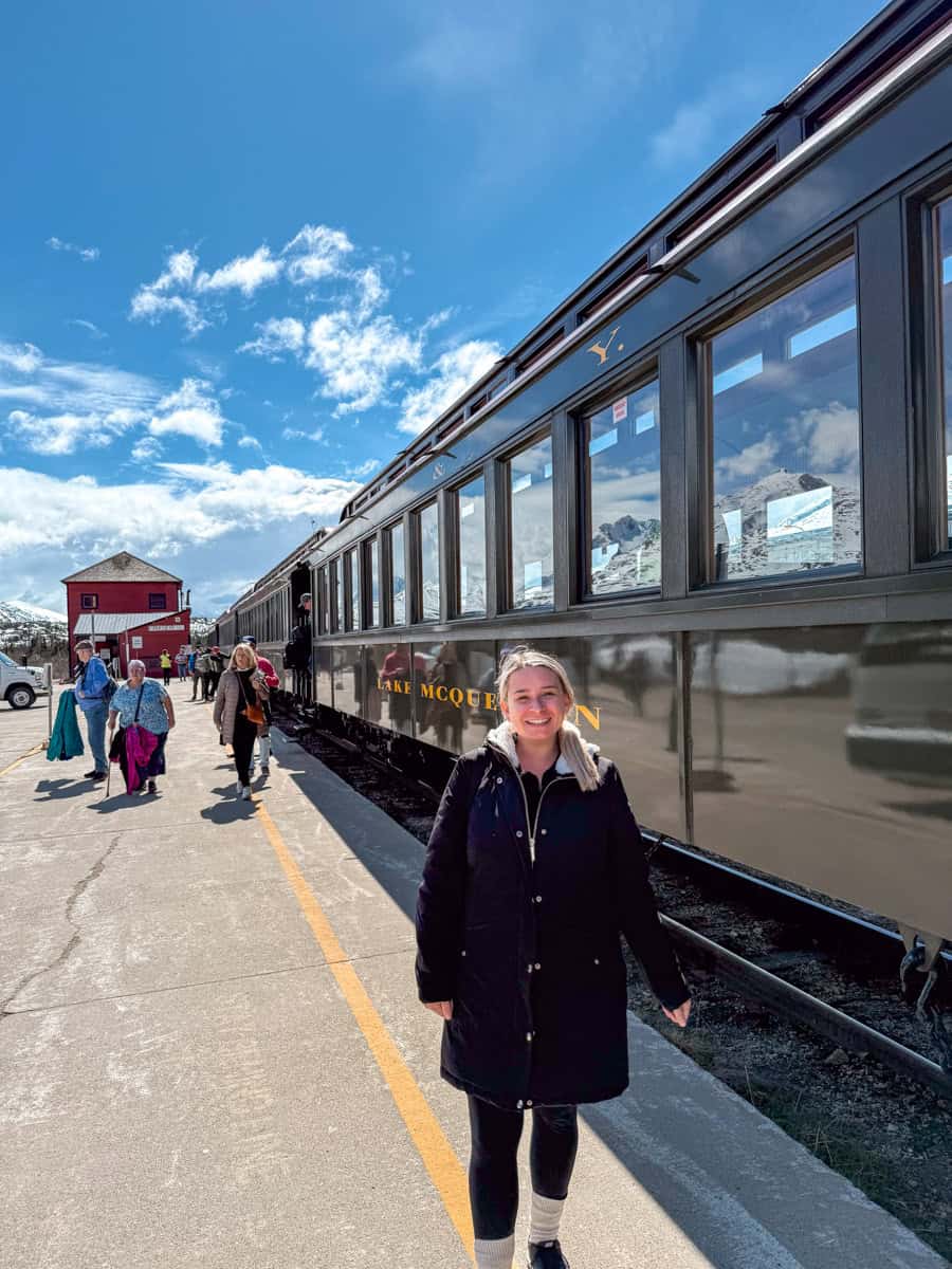 Eleanor is wearing layers while standing beside a train on a sunny day.
