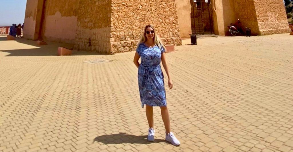 Photo of Eleanor wearing a blue tee shirt dress in front of a Moroccan kasbah