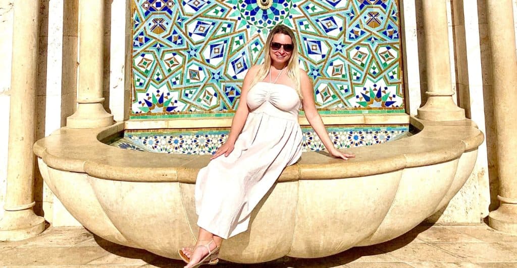 Photo of Eleanor wearing a tan dress in front of a Moroccan water fountain